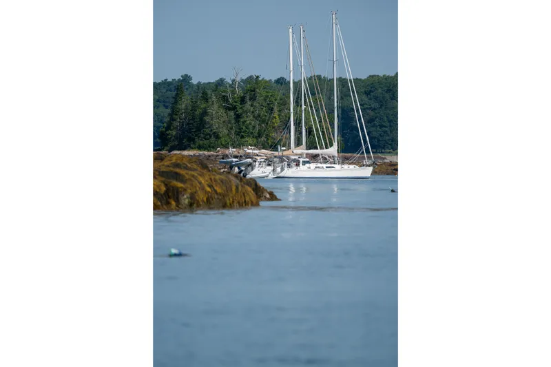 Slide: The Image of Sailboat Outbound 46, 2024 model, anchored near rocky shoreline with forested background. - 76