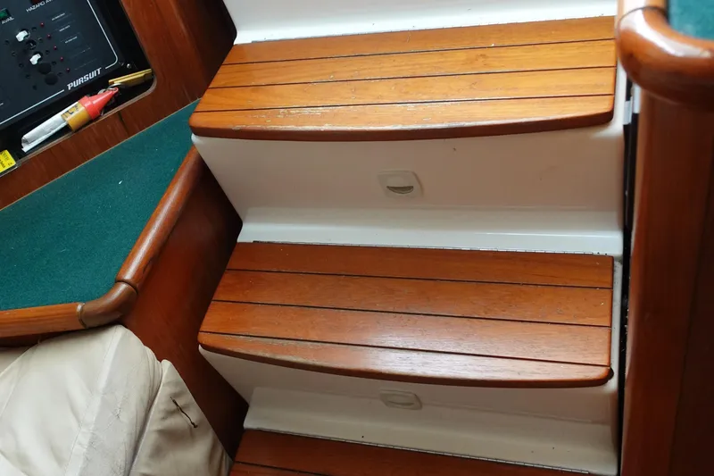 Slide: The Image of Wooden steps inside a 1997 Pursuit 3400 Offshore boat, featuring a control panel and green carpet. - 22