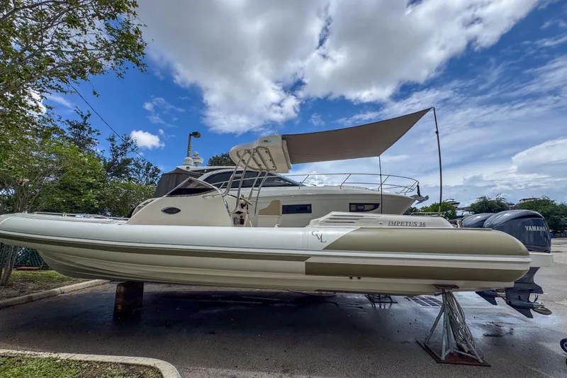 Slide: The Image of 2023 Tender Impertus 36 boat with canopy, parked outdoors under a cloudy sky. - 5