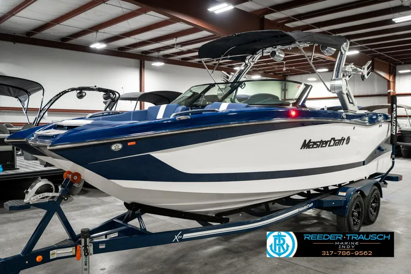 Slide: The Image of 2025 MasterCraft X24 boat in showroom, blue and white design, on trailer. - 3