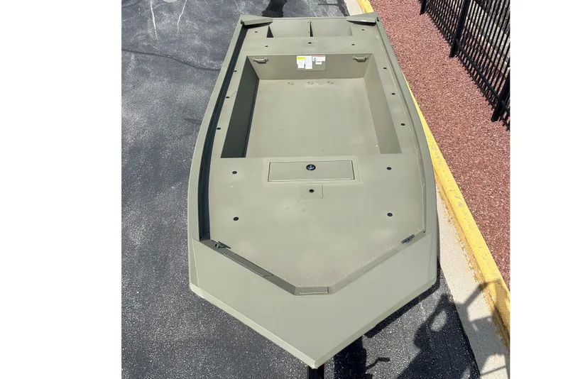 Slide: The Image of 2026 Tracker Grizzly 1754 Utility boat, olive green, on pavement near a fence. - 2
