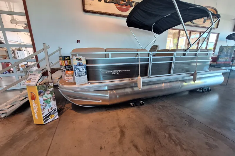 The Image of 2025 Sun Tracker Party Barge 20 DLX pontoon boat displayed indoors with promotional materials. - 0