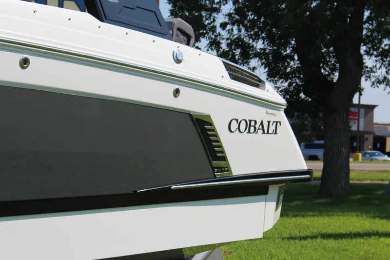 Slide: The Image of 2025 Cobalt R4 Surf boat, sleek design, parked on grass with trees in background. - 15
