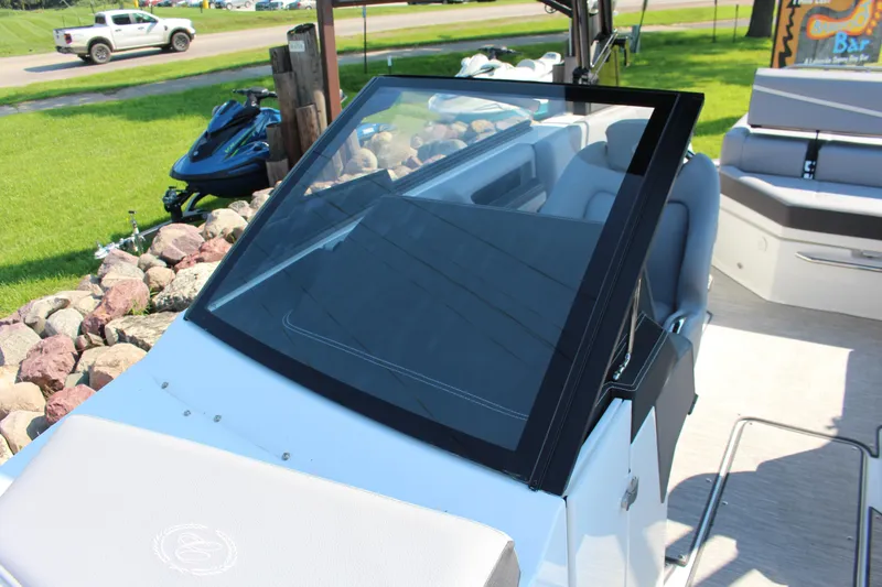 Slide: The Image of 2025 Cobalt R4 Surf boat interior with windshield and seating, parked near rocks and grass. - 33