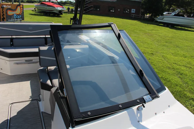 Slide: The Image of 2025 Cobalt R4 Surf boat interior with windshield, parked on grass near a lakeside bar. - 34
