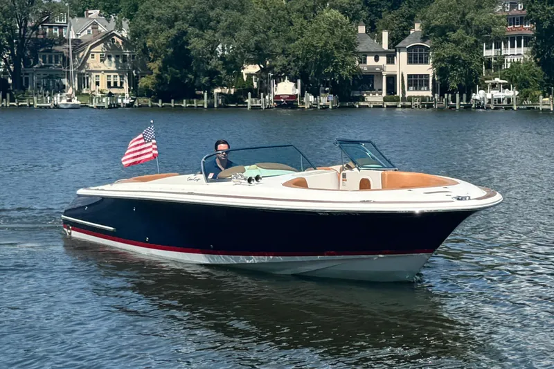 The Image of 2008 Chris-Craft Launch 28 boat cruising on a scenic lake with waterfront homes. - 0