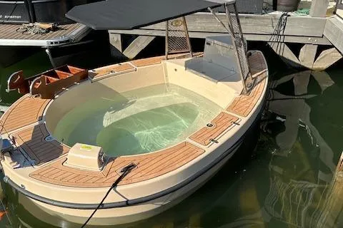 Slide: The Image of 2022 Spacruzzi V-1 boat with wooden deck and canopy, docked in calm water. - 2