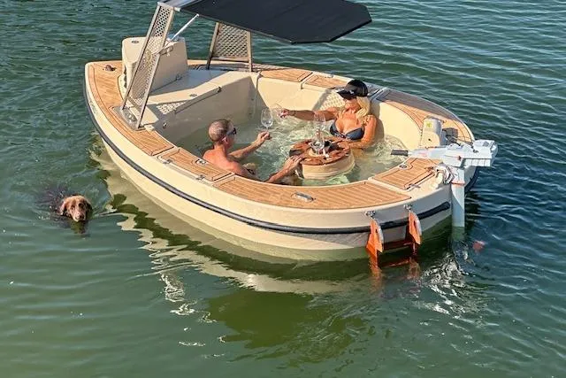 Slide: The Image of 2022 Spacruzzi V-1 boat with hot tub, two people relaxing, and a dog swimming nearby. - 5