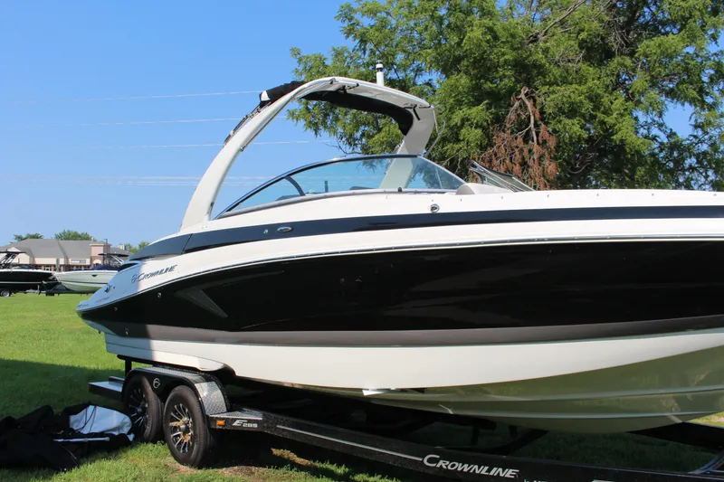 Slide: The Image of 2023 Crownline E285 boat on trailer, parked on grass with trees in background. - 30
