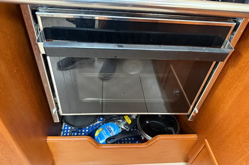 Slide: The Image of 2008 Island Packet 370 galley with oven and storage, featuring cleaning supplies and cookware. - 53