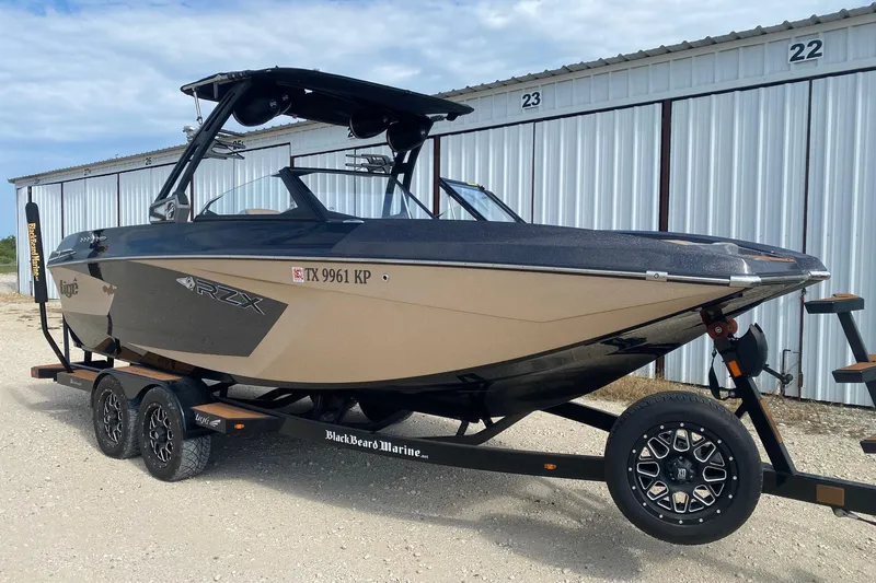 Slide: The Image of 2021 Tigé 23RZX boat on trailer, parked near storage units. - 1