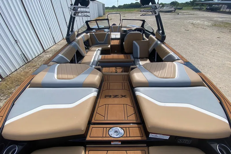 Slide: The Image of 2021 Tigé 23RZX boat interior with tan and gray seating, docked outdoors. - 10