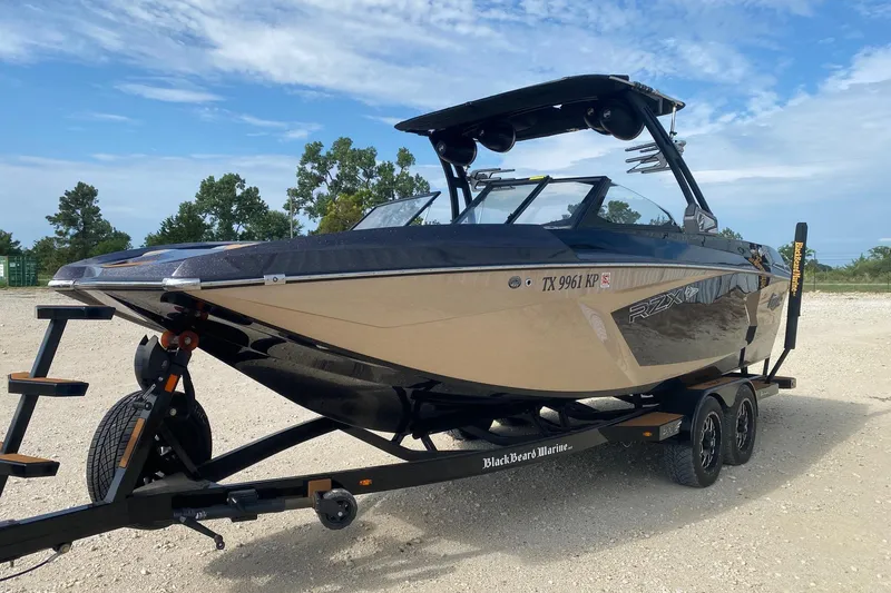 Slide: The Image of 2021 Tigé 23RZX boat on trailer, parked outdoors with trees in background. - 2