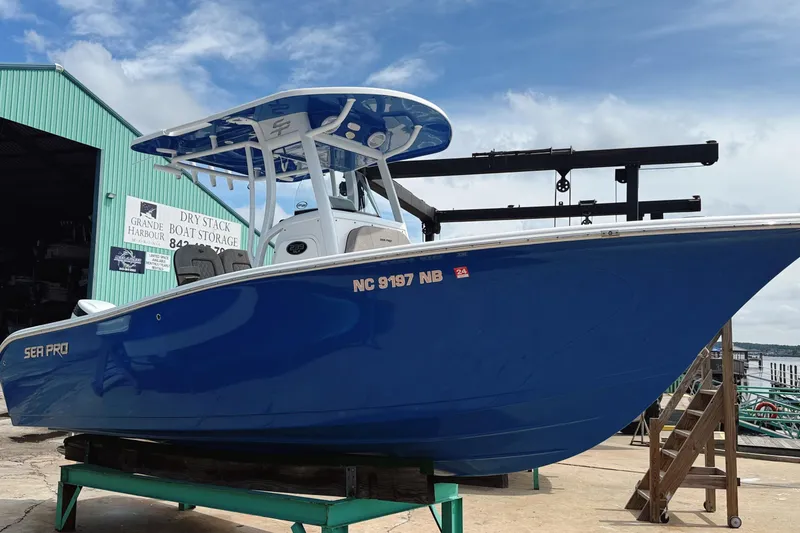 Slide: The Image of 2023 Sea Pro 239 DLX boat in blue, docked at a marina under a clear sky. - 2