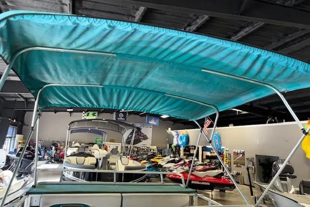 Slide: The Image of 1997 Crest Sport boat with teal canopy in showroom, surrounded by other watercraft. - 16