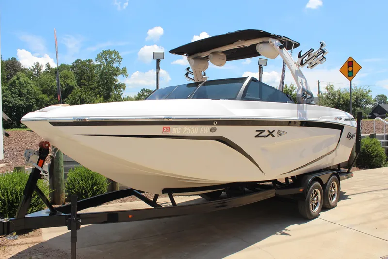Slide: The Image of 2021 Tigé 23ZX boat on trailer, sleek design, sunny day background. - 2
