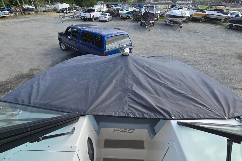 Slide: The Image of 2020 Twin Vee 240 DC GF boat with cover, parked near blue SUV in a boatyard. - 66