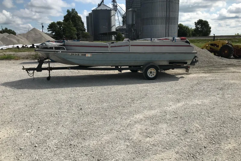 Slide: The Image of 1991 Lowe 2200 boat on trailer, parked on gravel with industrial background. - 2