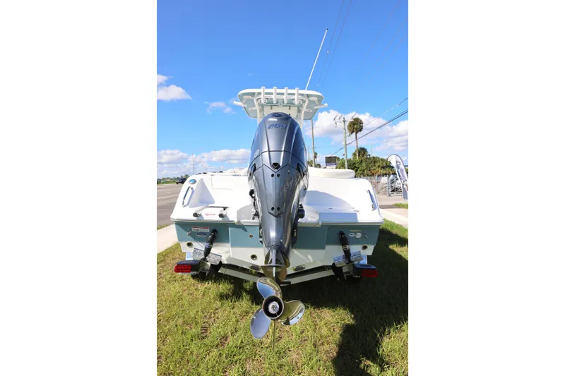 Slide: The Image of 2026 Sea Hunt Ultra 229 boat with powerful outboard motor, parked on grass under clear blue sky. - 20