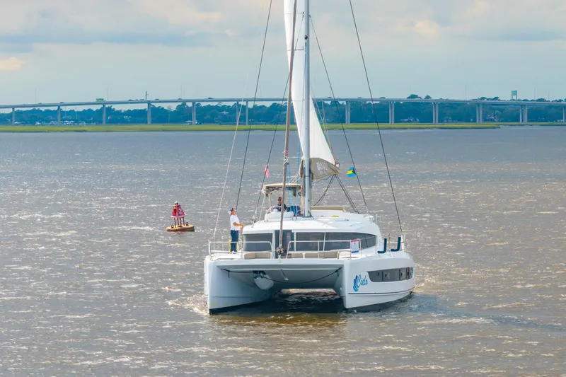 Slide: The Image of 2023 Bali 4.2 catamaran sailing on a river with a bridge in the background. - 113
