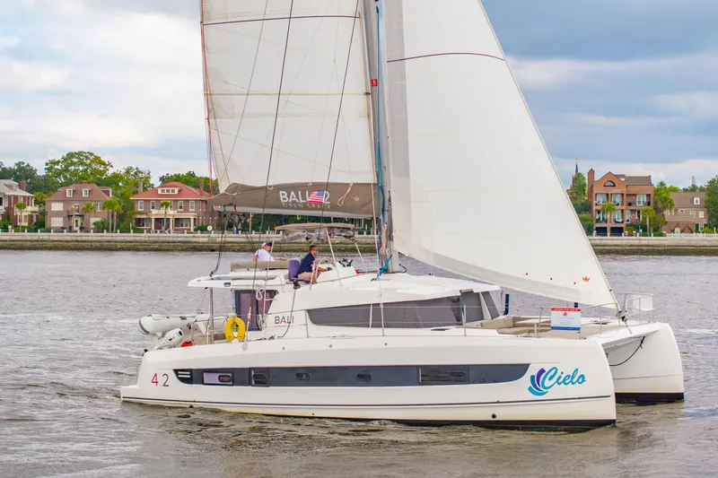 Slide: The Image of 2023 Bali 4.2 catamaran sailing near waterfront homes under cloudy skies. - 4