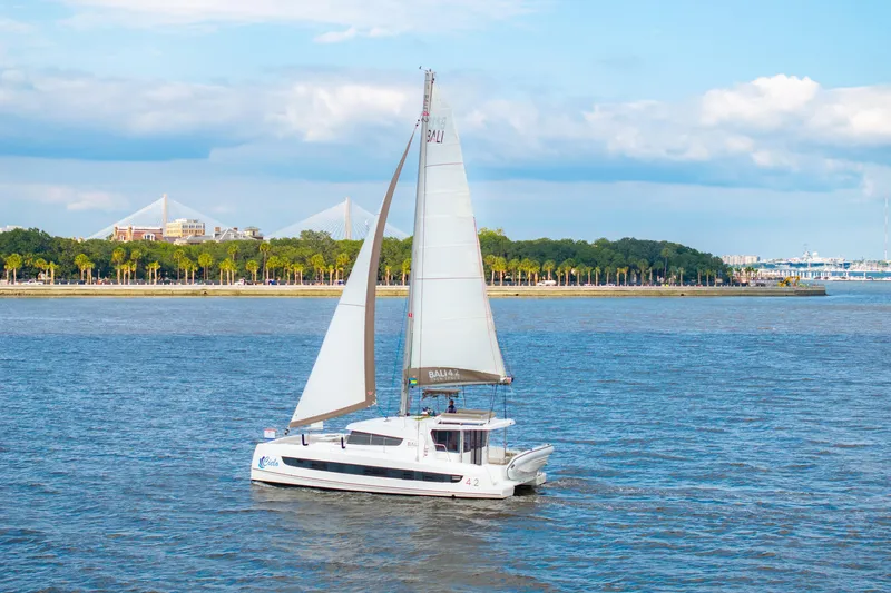 Slide: The Image of Sailing catamaran Bali 4.2, 2023 model, cruising on a scenic river with bridge view. - 5
