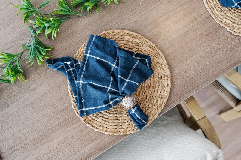 Slide: The Image of Woven placemat with blue checkered napkin on wooden table, surrounded by greenery. - 59