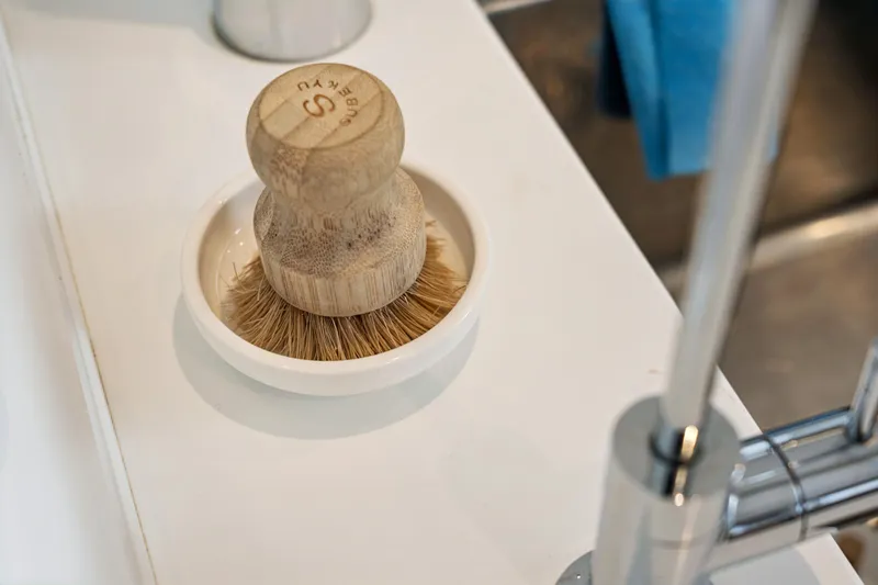 Slide: The Image of Wooden dish brush on a white kitchen countertop near a modern faucet. - 67