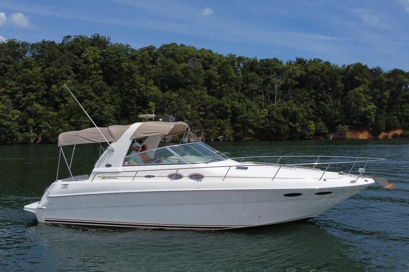 The Image of 2001 Sea Ray 310 Sundancer cruising on a serene lake with lush forest backdrop. - 0