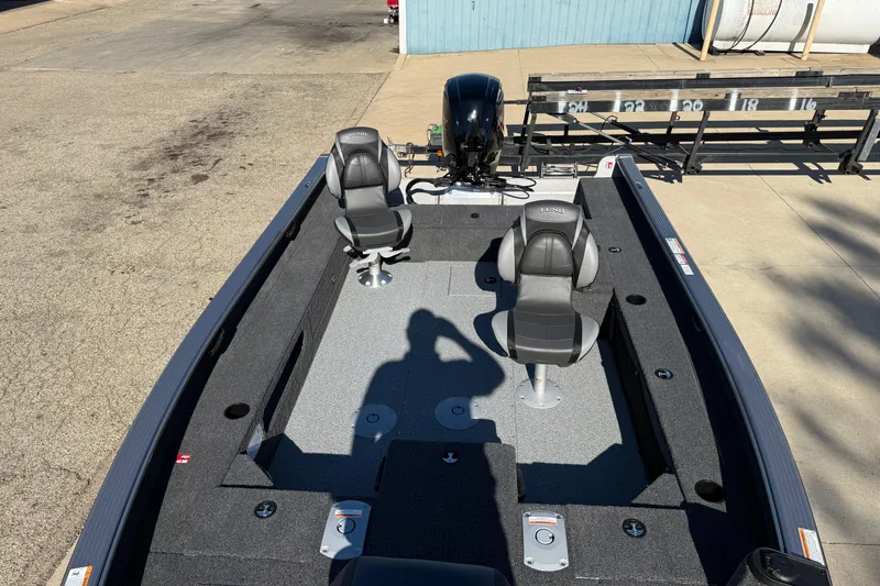 Slide: The Image of 2026 Lund 1875 Pro Guide fishing boat with dual seats and motor, parked on concrete. - 9