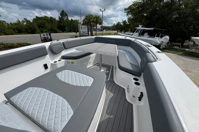Slide: The Image of 2026 NauticStar 332 Offshore boat interior with gray seating and table, parked outdoors. - 18