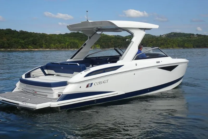 Slide: The Image of 2023 Cobalt A29 boat cruising on a serene lake with lush green shoreline. - 2