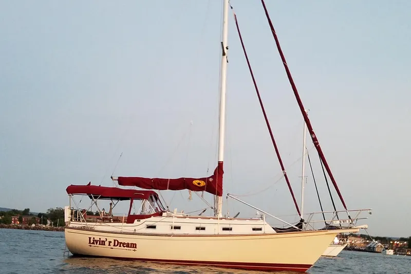The Image of 1990 Island Packet 32 sailboat with red sails on calm water. - 0
