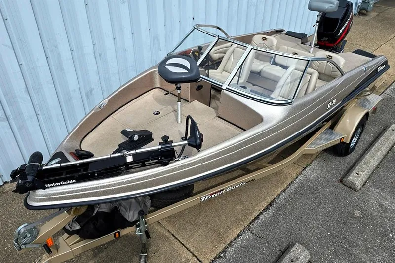 Slide: The Image of 2005 Triton SF18 F&S boat with MotorGuide, parked on a trailer near a blue wall. - 2