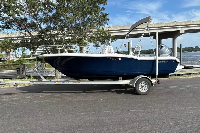 Slide: The Image of 2017 Tidewater 180 CC Adventure boat on trailer by riverside, under a bridge. - 1