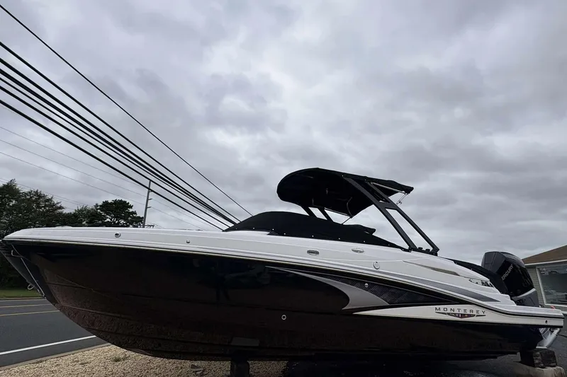 Slide: The Image of 2026 Monterey M65 boat with sleek design, parked on gravel under cloudy sky. - 2