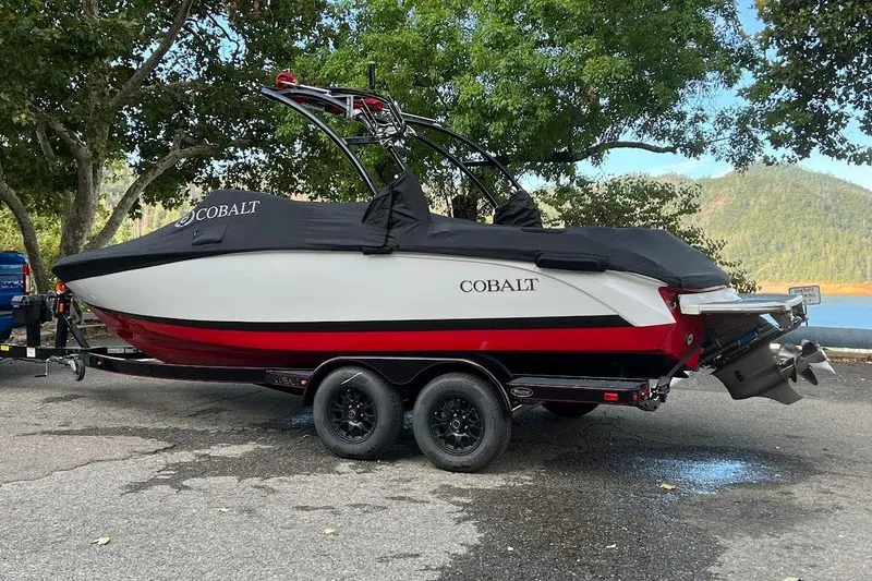 Slide: The Image of 2017 Cobalt 220S boat on trailer, covered, parked near trees and water. - 16