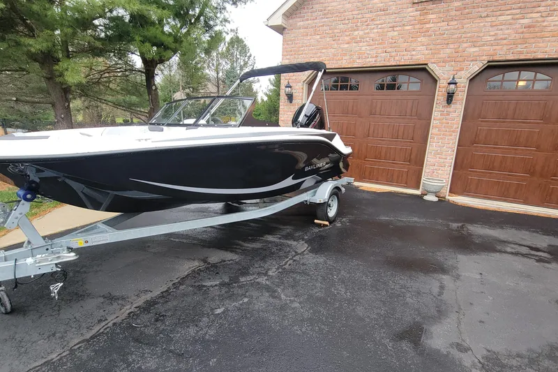 Slide: The Image of 2025 Bayliner Element M17 boat on trailer, parked in driveway near brick garage. - 2