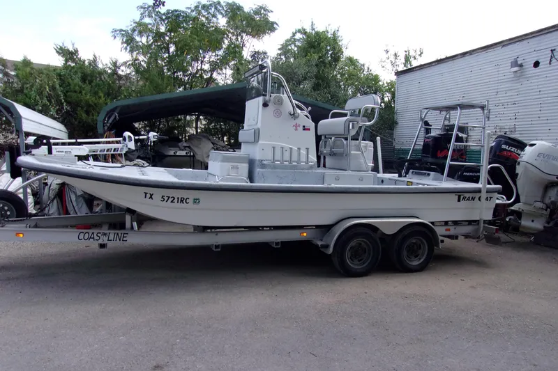 Slide: The Image of 2004 Tran Cat 21 boat on trailer, parked outdoors with trees and building in background. - 1