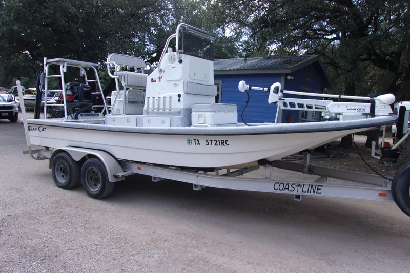 Slide: The Image of 2004 Tran Cat 21 boat on trailer, parked outdoors near trees and a blue building. - 2