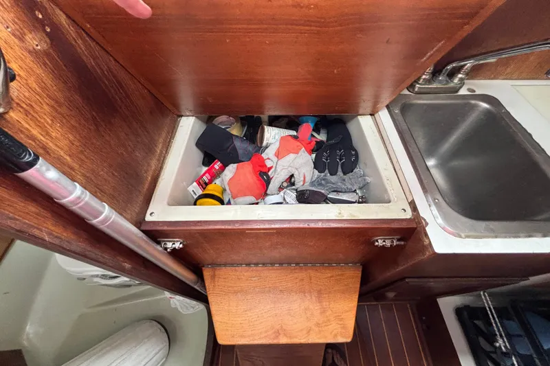 Slide: The Image of Storage compartment on 1988 J Boats J/28 sailboat, filled with various items, next to sink. - 28