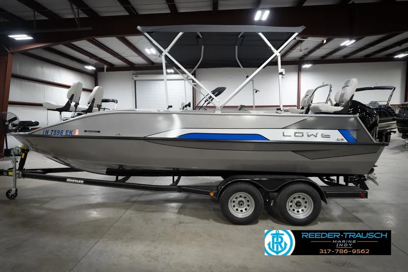 Slide: The Image of Silver Lowe boat on trailer in indoor showroom, featuring blue accents and seating. - 9