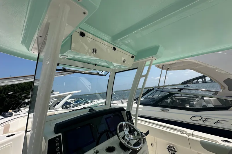 Slide: The Image of 2023 Robalo R302 Center Console boat interior with steering wheel and electronics, docked near other boats. - 12