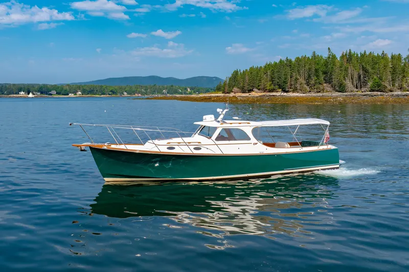 Slide: The Image of 1999 Hinckley Picnic Boat cruising on serene waters with forested shoreline backdrop. - 2
