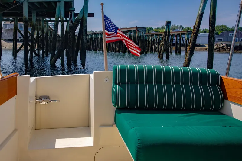 Slide: The Image of 1999 Hinckley Picnic Boat interior with green striped seating, American flag, and dock view. - 24