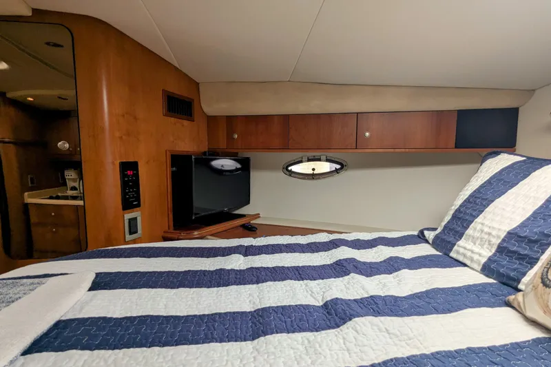 Slide: The Image of 2000 Cruisers Yachts 3870 Express cabin with striped bedding and wall-mounted TV. - 25