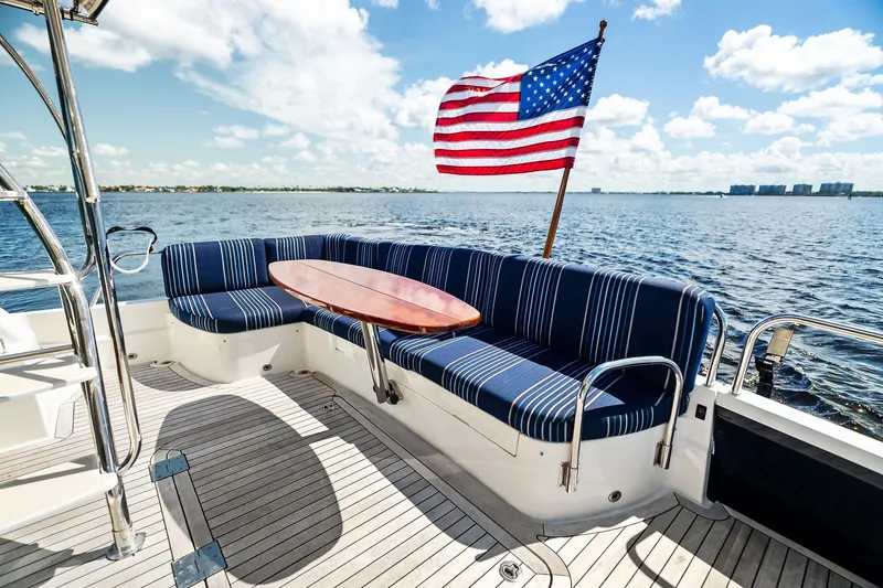 Slide: The Image of 2019 Sabre Flybridge yacht deck with striped seating and American flag, overlooking serene waters. - 5