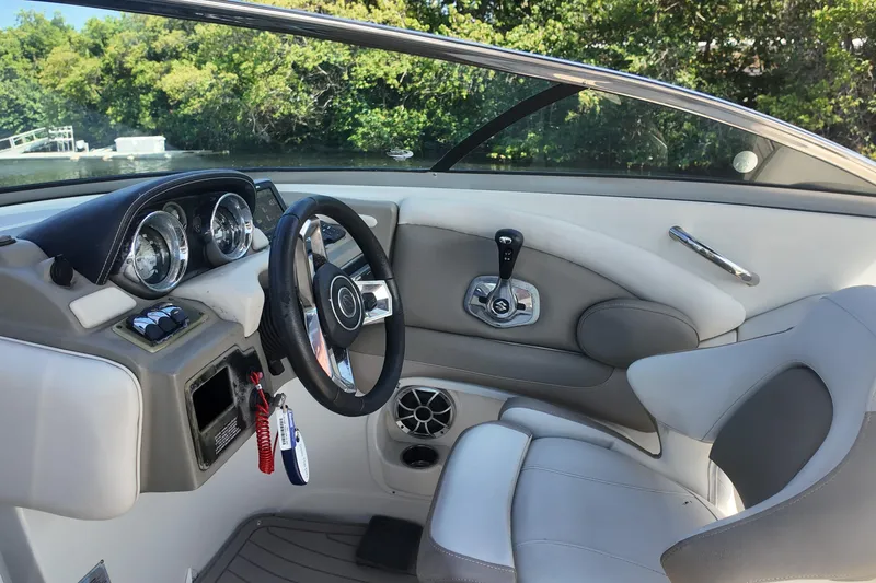 Slide: The Image of 2020 Crownline 24 boat interior with steering wheel and dashboard, surrounded by lush greenery. - 14