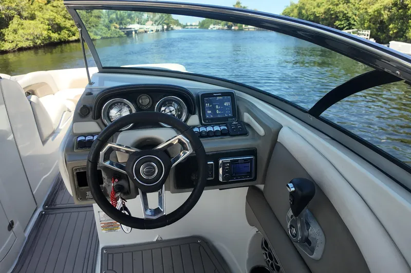 Slide: The Image of 2020 Crownline 24 boat dashboard with steering wheel and navigation controls on a scenic waterway. - 15