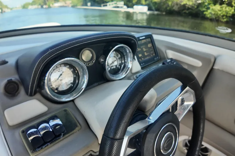 Slide: The Image of 2020 Crownline 24 boat dashboard with steering wheel and gauges on a scenic waterway. - 16